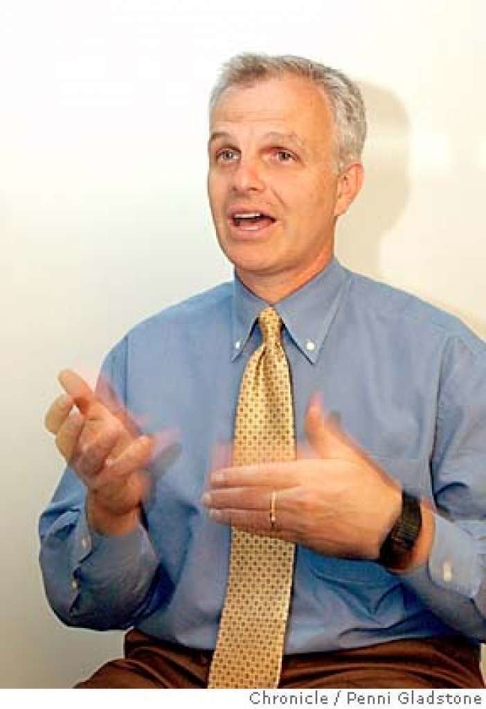 David Neeleman wearing blue long sleeves, a yellow tie, brown pants, a black watch, and a ring.