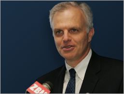 David Neeleman wearing a black suit, white shirt, and a blue tie during an interview.