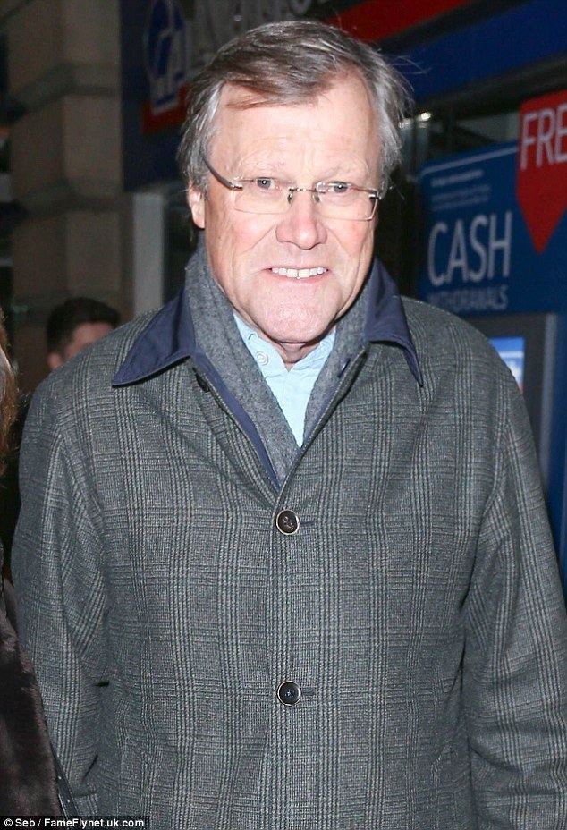 David Neilson smiling while wearing a gray and black checkered coat, blue long sleeves, and eyeglasses