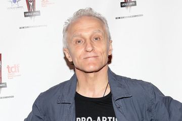 David Patrick Kelly smiling closed mouth while wearing a black shirt underneath a gray jacket.