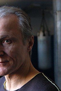 David Patrick Kelly smiling on his side inside a gym and wearing a black shirt.