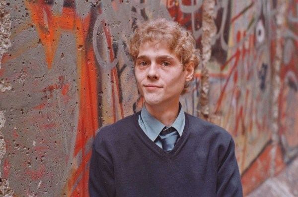 David Reimer smiling and wearing a blue sweatshirt over a gray long sleeves and neck tie.