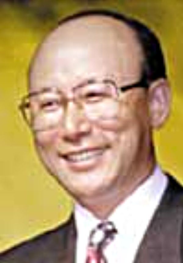 David Yonggi Cho smiling and wearing a black coat over a white formal suit with a balder head.