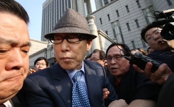 David Yonggi Cho being flocked by interviewers and wearing a brown hat and blue formal attire.