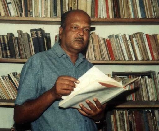 Dayananda Gunawardena wearing gray polo shirt while holding a book in a Library