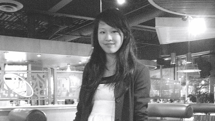 Elisa Lam smiling while standing and wearing a white blouse and coat inside the hotel