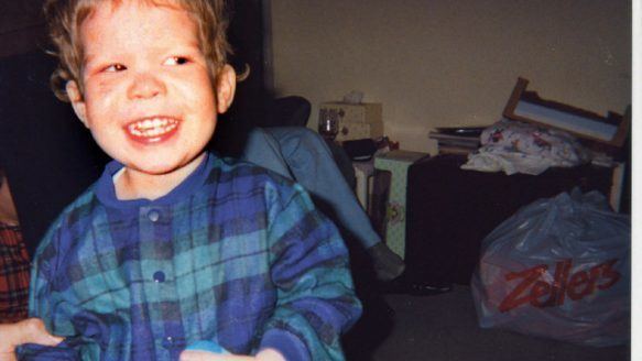 Jeffrey Baldwin is happy, standing in a room with a black table at the back and a plastic bag, mouth half open, looking to his left, has brown hair, wearing a blue checkered long sleeve polo.