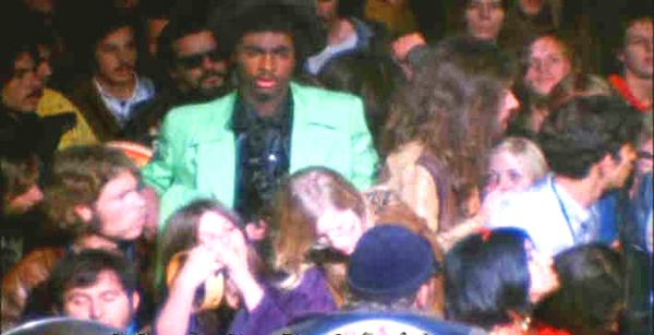 Meredith Hunter wearing a mint green coat and a black shirt surrounded by people.