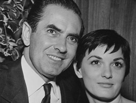 Deborah Minardos with her husband Tyrone Power wearing a white shirt, a coat, and a tie