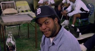 Ice Cube as Doughboy in the 1991 film Boyz n the Hood with a smiling face, wearing a cap and a blue polo shirt.