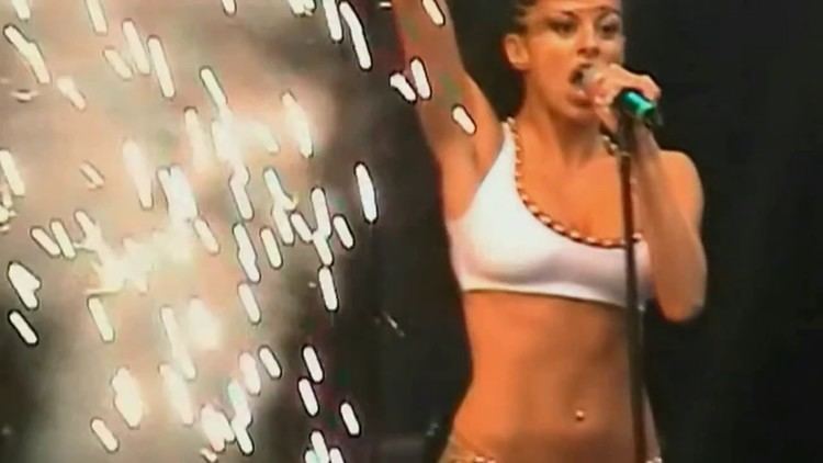 Dee Demirbag wearing sexy white outfit with gold details while holding  microphone