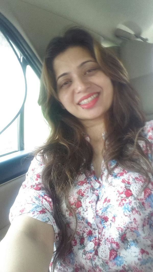 Deepali Sayed smiling inside a car, with wavy long hair, and wearing a multi-colored floral long sleeve top.