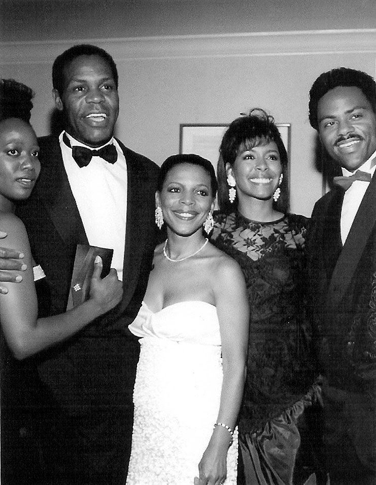 Denise Gordy smiling in the middle of a group of people in an event wearing a white dress.