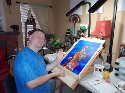 Derek Riggs with closed eyes while showing his painting, wearing a blue shirt, and gray shorts.