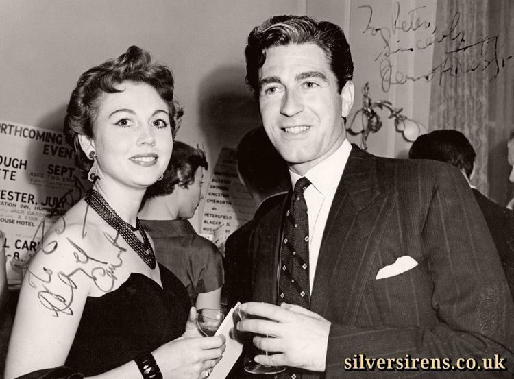 Dermot Walsh smiling and wearing a suit and tie with Hazel Court wearing a necklace and a black sexy dress.