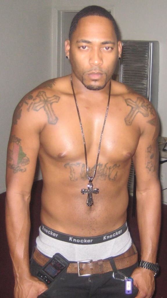 Desi Arnez Hines II showing his tattoos and wearing cross necklace, boxer short, brown belt and black pants