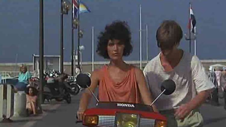 Caroline Tresca riding in a motorcycle with Philippe Caroit wearing striped t-shirt in a movie scene from Deux enfoirés à Saint-Tropez