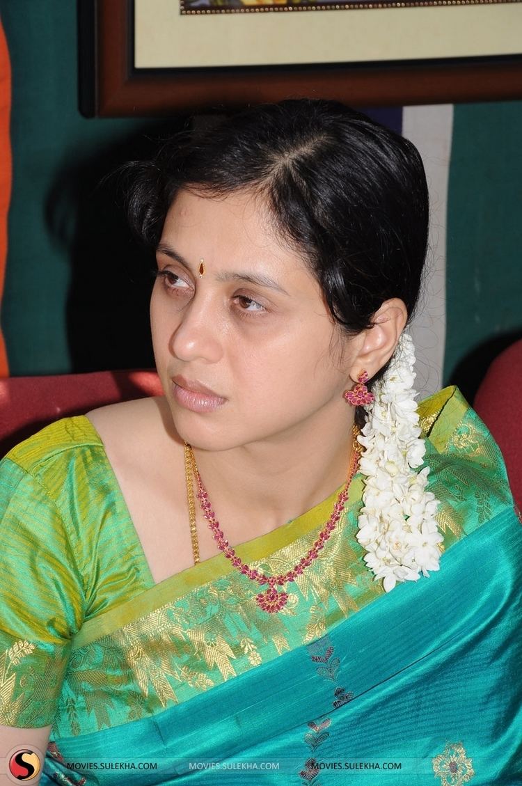 Devayani Jayadev with a flower on her hair, wearing earrings, a necklace, and a color green and blue dress.