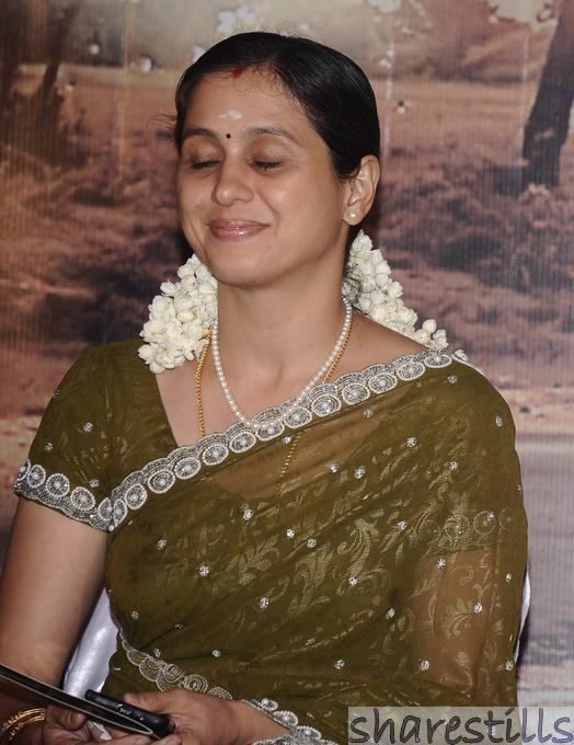 Devayani Jayadev wearing earrings, a necklace, bracelets, and a green dress while holding gadgets.