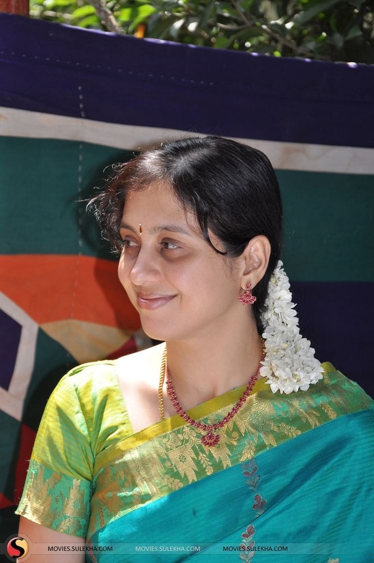 Devayani Jayadev with a flower on her hair, wearing earrings, a necklace, and a color green and blue dress.