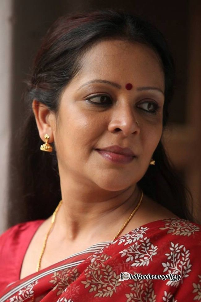 Devi Ajith smiling and wearing a red saree, dangling earrings and necklace with a red mark on the forehead