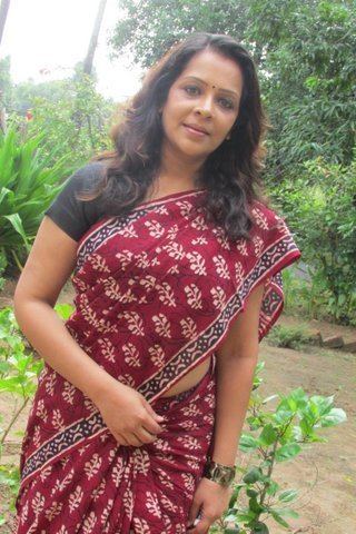 Devi Ajith smiling with her wavy hair down and wearing a red saree