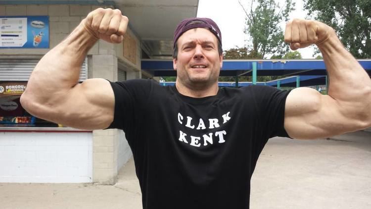 Devon Larratt showing his muscle while wearing black printed shirt and violet cap