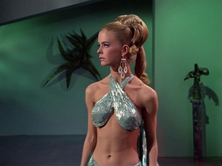 Diana Ewing as Droxine with a serious face, blonde hair, wearing chandelier earrings, and a sexy mint green top in a scene from Star Trek (1966–1969 film).