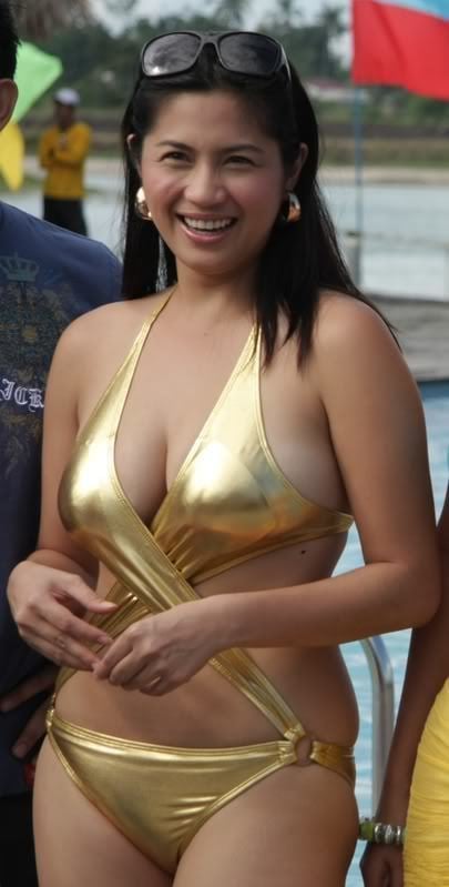 Diana Zubiri laughing while wearing a golden bikini, earrings, and black sunglasses on the top of her head
