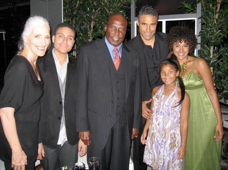 Dianne Gerace with curly hair, wearing a sexy green dress with her husband, Ulrich Fox wearing a black suit, and her daughter wearing a sleeveless dress together with a lady wearing a black dress and two gentlemen wearing a black suit.