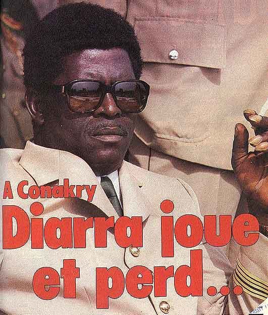 Diarra Traoré sitting while wearing a white shirt, a coat, a tie, and pair of sunglasses