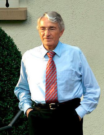 Dieter Schwarz' hands on his pocket while wearing blue long sleeves, necktie, black pants, and eyeglasses