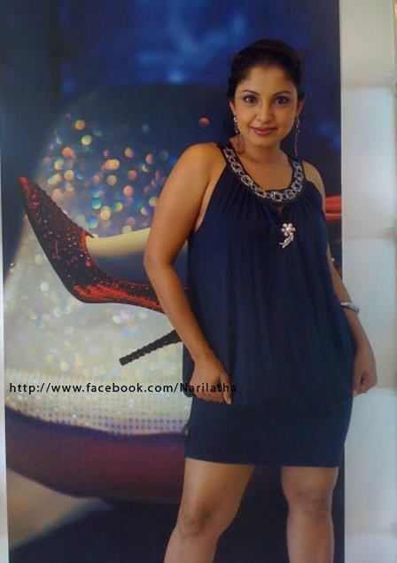 Dilhani Ekanayake with a tight-lipped smile while wearing a blue sleeveless dress, earrings, necklace, and bracelet