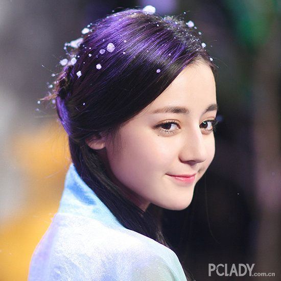 Dilraba Dilmurat with a tight-lipped smile and an updo hairstyle while wearing a white blouse