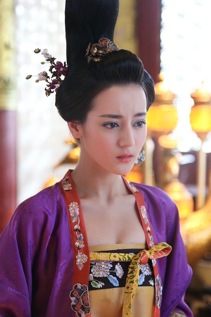 Dilraba Dilmurat with a serious face while wearing a red and violet robe, black and yellow inner blouse, and floral hair accessory