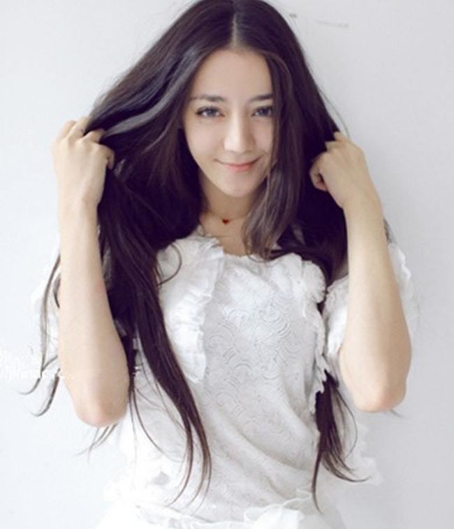 Dilraba Dilmurat smiling while holding her hair and wearing a white blouse