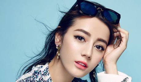 Dilraba Dilmurat holding the sunglasses on her head while wearing a white and blue long sleeve blouse and earrings