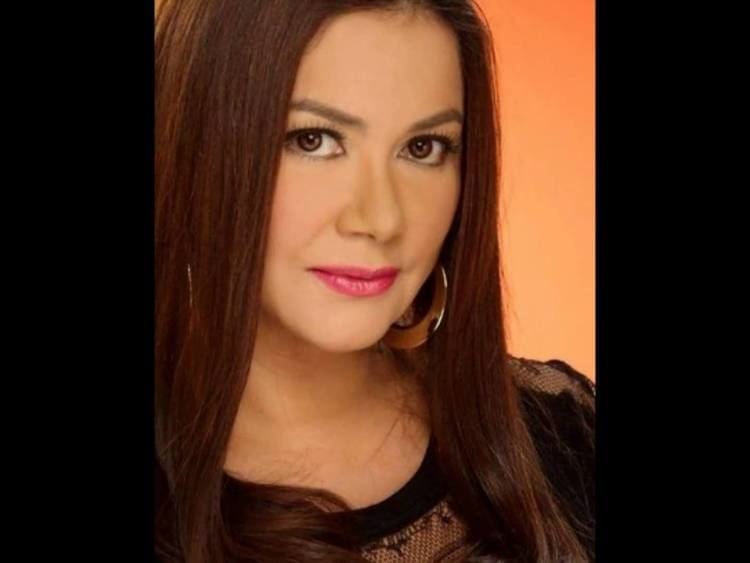 Dina Bonnevie with a tight-lipped smile while wearing a black lace blouse and earrings
