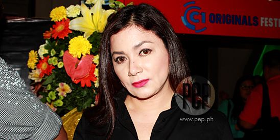 Dina Bonnevie posing with flowers at her back and she is wearing a black blouse