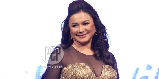 Dina Bonnevie smiling while wearing a gold sequin dress with a black net and earrings