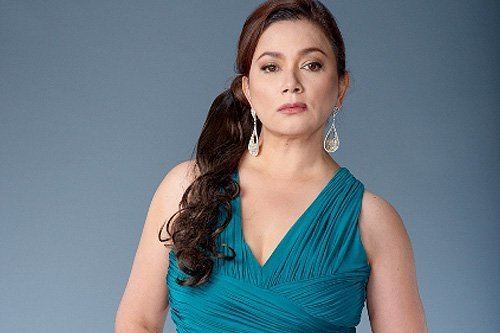 Dina Bonnevie with a fierce look while wearing a blue sleeveless dress and earrings