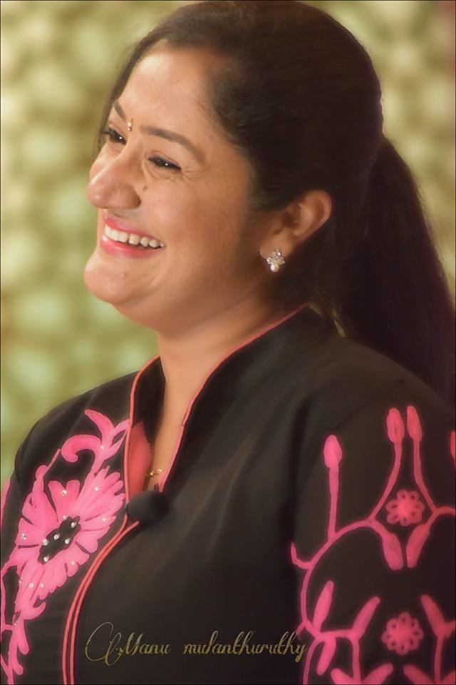 Dini Daniel smiling for the camera wearing a black dress with pink flower designs.