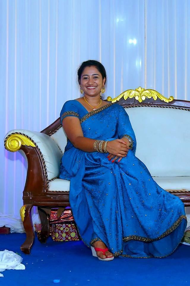 Dini Daniel Malayalam Serial sitting down while smiling and wearing a blue Sri Lankan dress and jewelry.