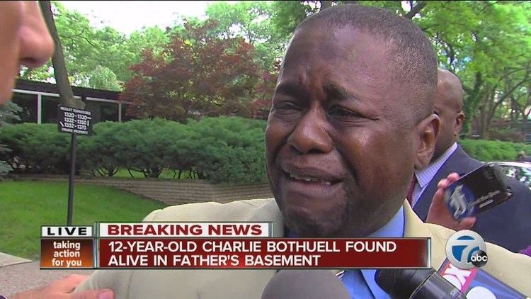 In a report, Charlie Bothuell IV is crying and has black hair, and a lot of microphones in front, below is the headline of the news, he is wearing blue long sleeves under a tan-colored suit.