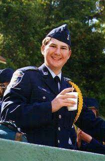 Zebb Quinn smiling while holding a plastic cup and wearing a blue coat, blue cap, white long sleeves, and necktie