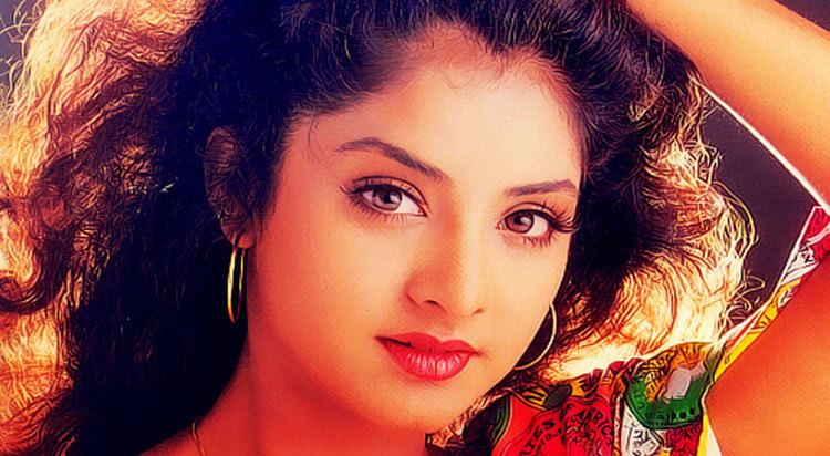 Divya Bharti with curly hair, wearing earrings, a necklace, and a colorful top.