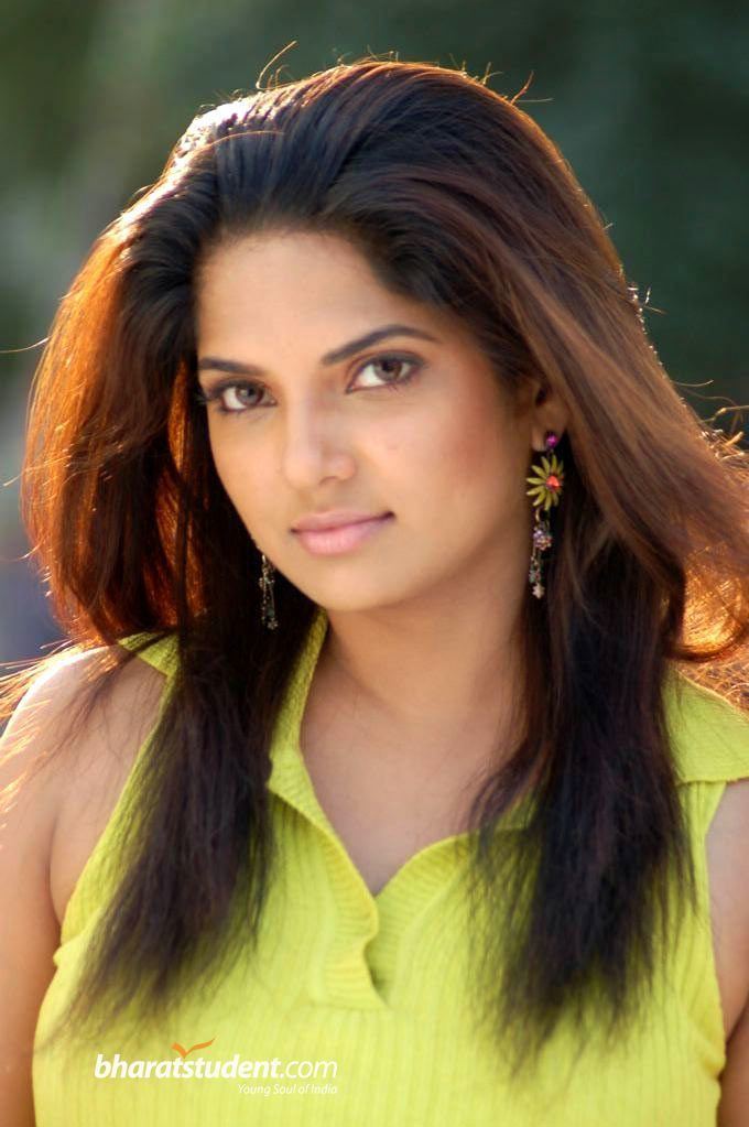 Diya with a tight-lipped smile while wearing a yellow-green sleeveless blouse and earrings
