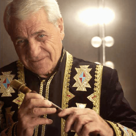 Djivan Gasparyan smiling while holding the flute and wearing a black and gold long sleeves