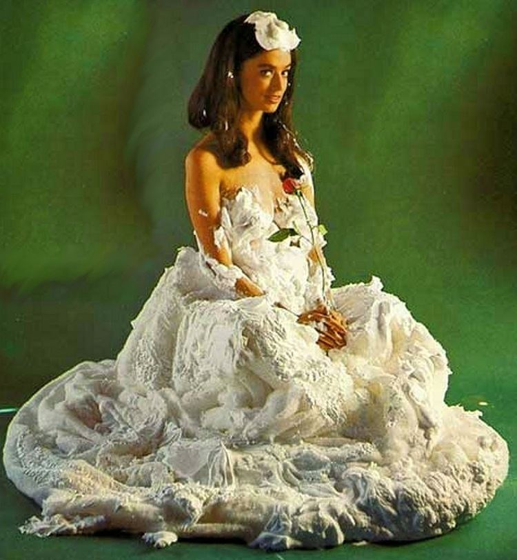 Dolores Erickson smiling while holding a rose and wearing a gown covered with whipped cream