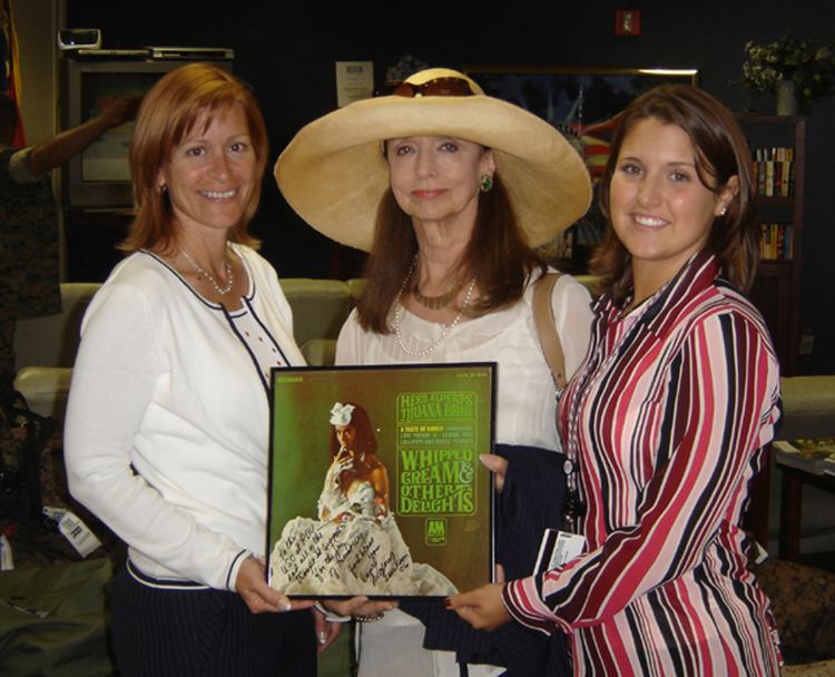 Dolores Erickson, at the center, smiling while holding the album cover of Whipped Cream & Other Delights, with the two women beside her